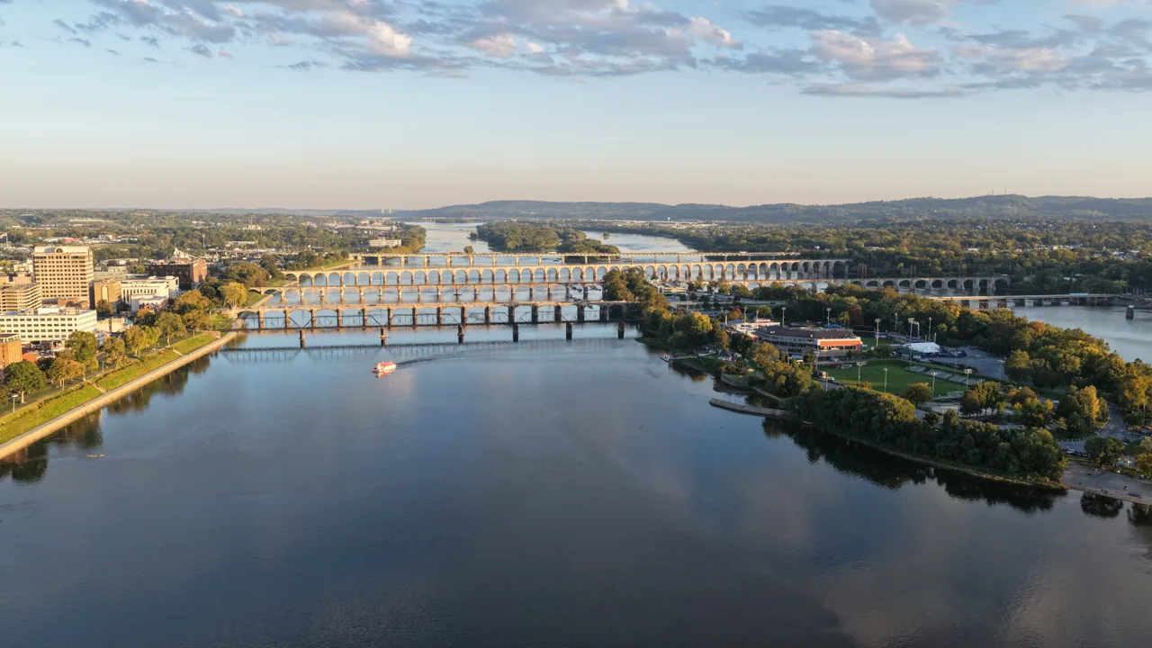 A wide aerial view along the Susquehanna River toward a series of bridges and the Harrisburg shoreline